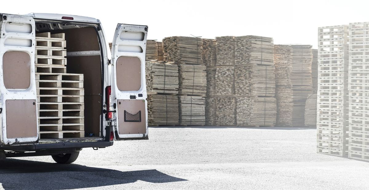 Een witte bestelwagen met open achterdeuren, geladen met houten paletten
