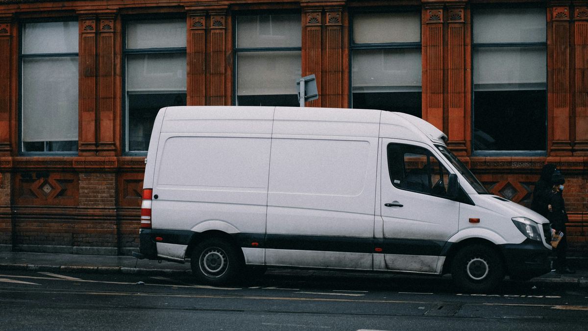 Een witte bestelwagen langs de stoep voor een gevel van rode baksteen